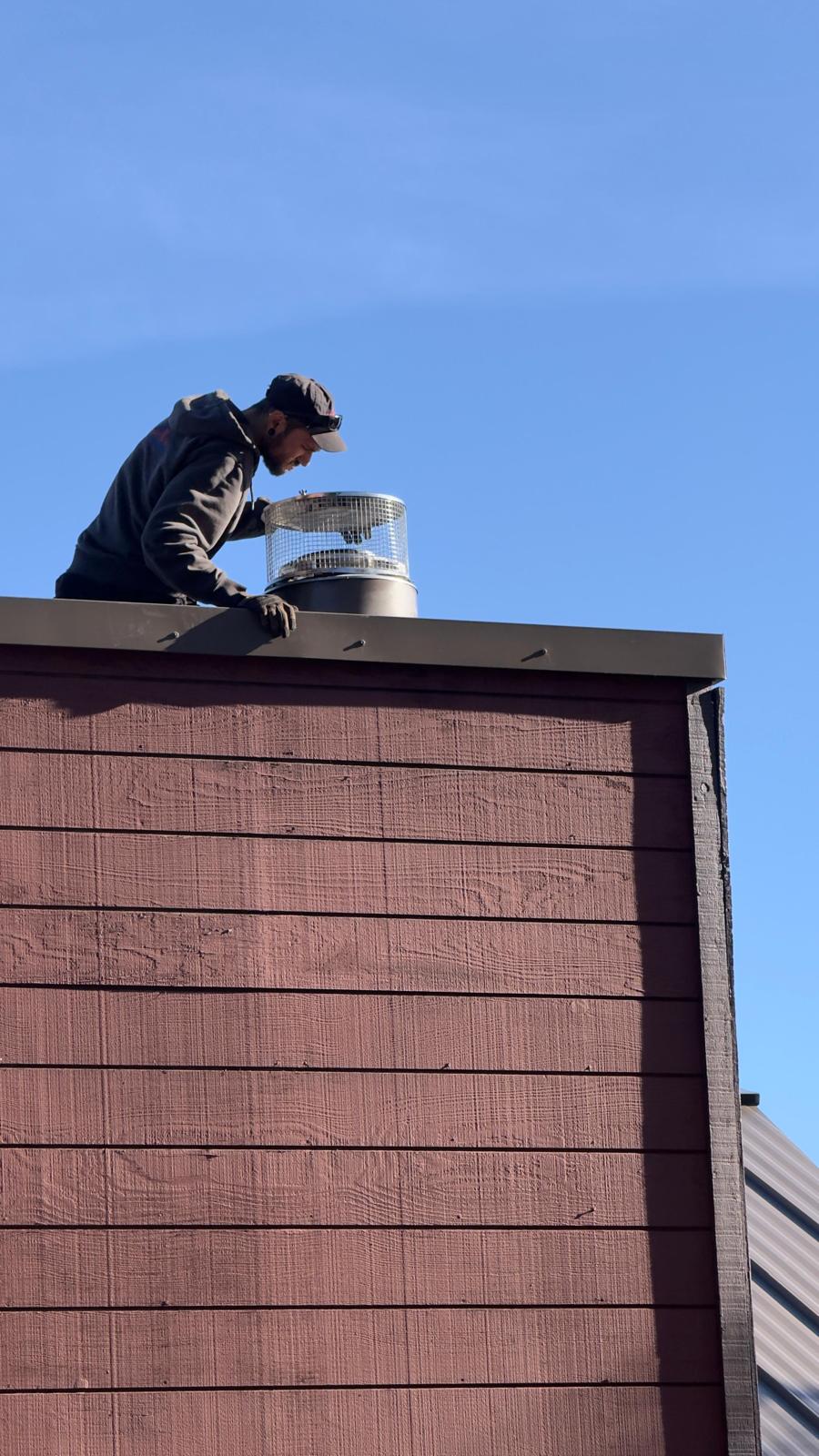 Michael leaning over a dark chase top with both hands on a stainless mesh-sided chimney cap