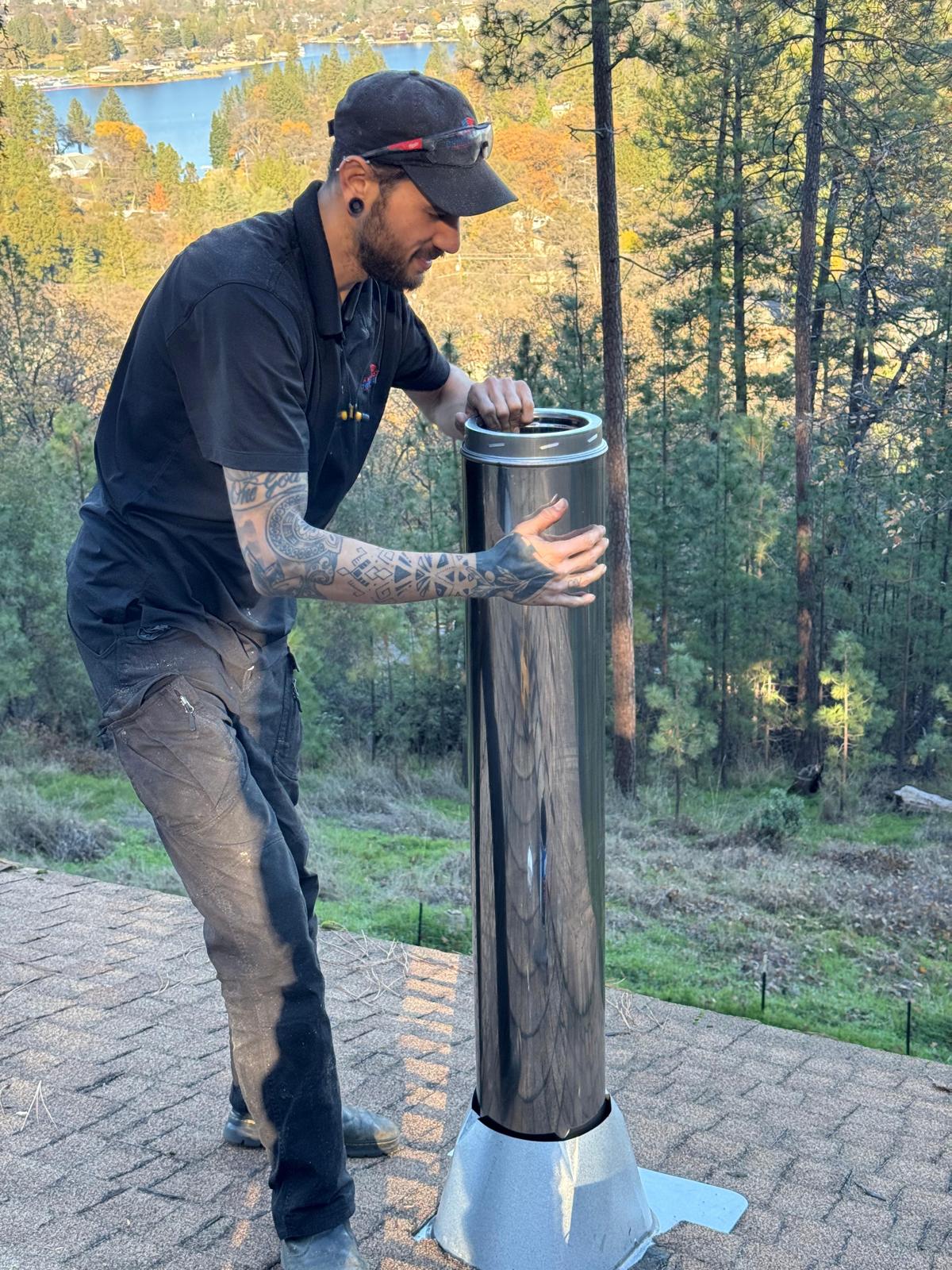 Michael seating a polished stainless double-wall chimney pipe into flashing on a shingle roof