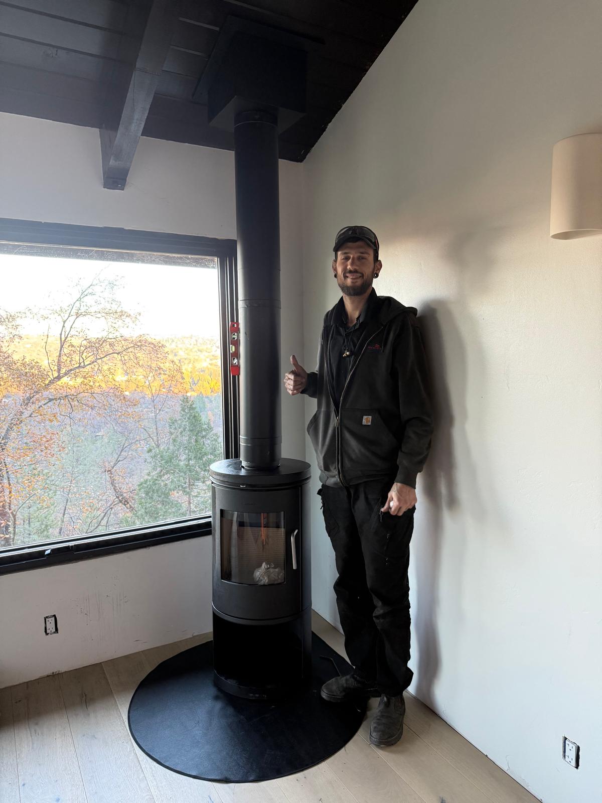 Michael standing beside a black wood stove with a magnetic level on the stovepipe