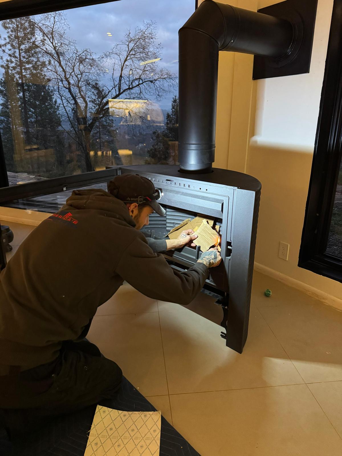 Michael kneeling and lighting a paper starter inside a modern black stove or insert