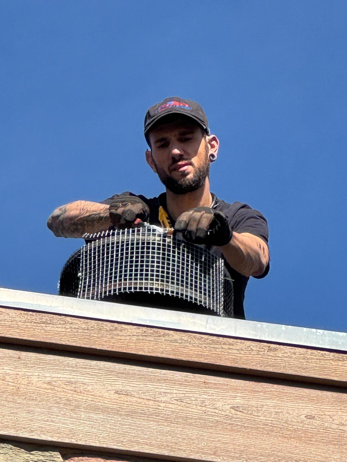 Michael at a chase top holding a stainless mesh chimney cap in gloved hands