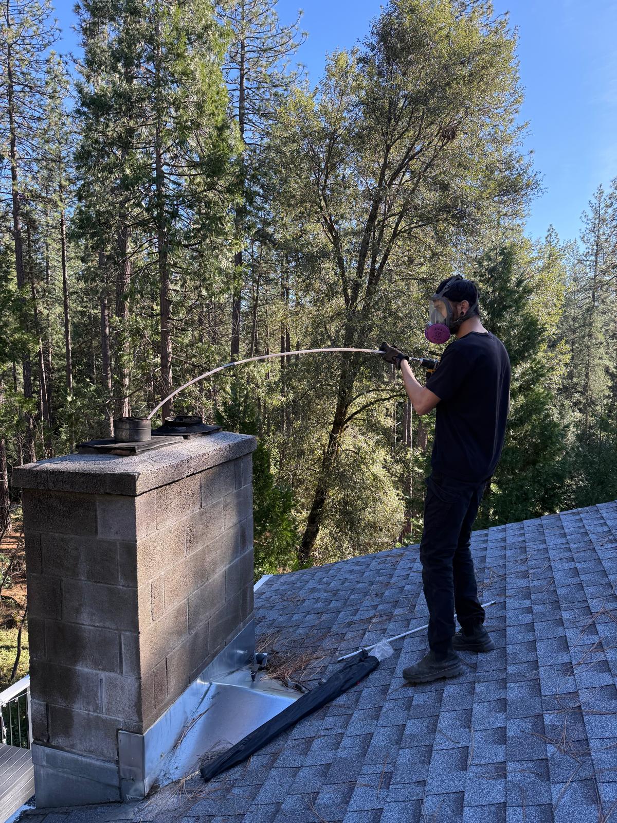 Michael wearing a full-face respirator and spraying toward a concrete-block chimney top