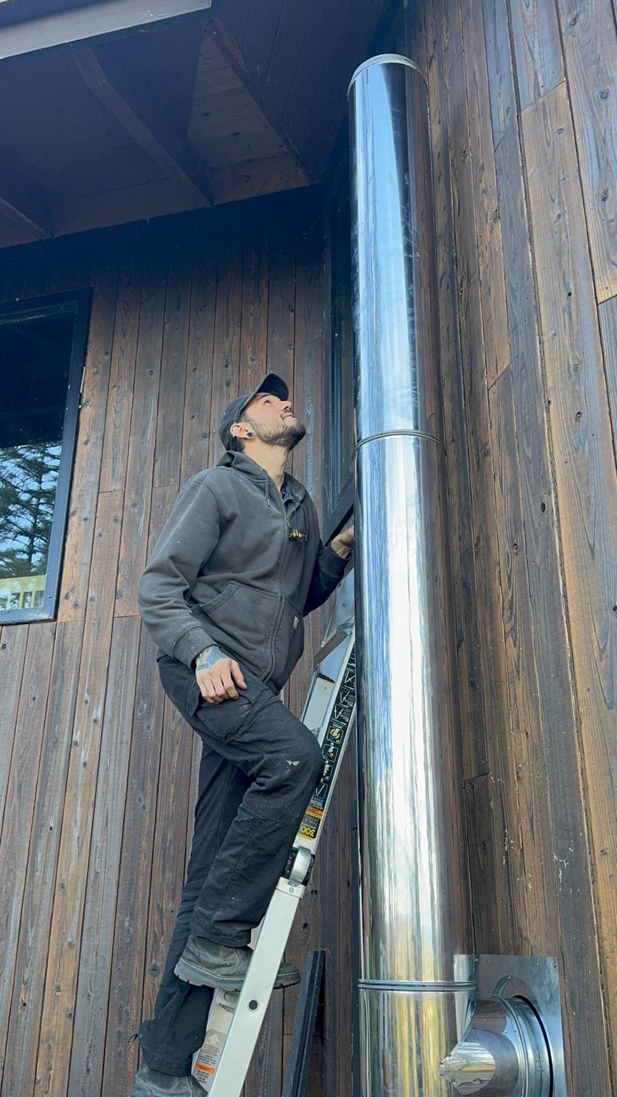 Michael on an aluminum ladder looking up a stainless exterior chimney pipe