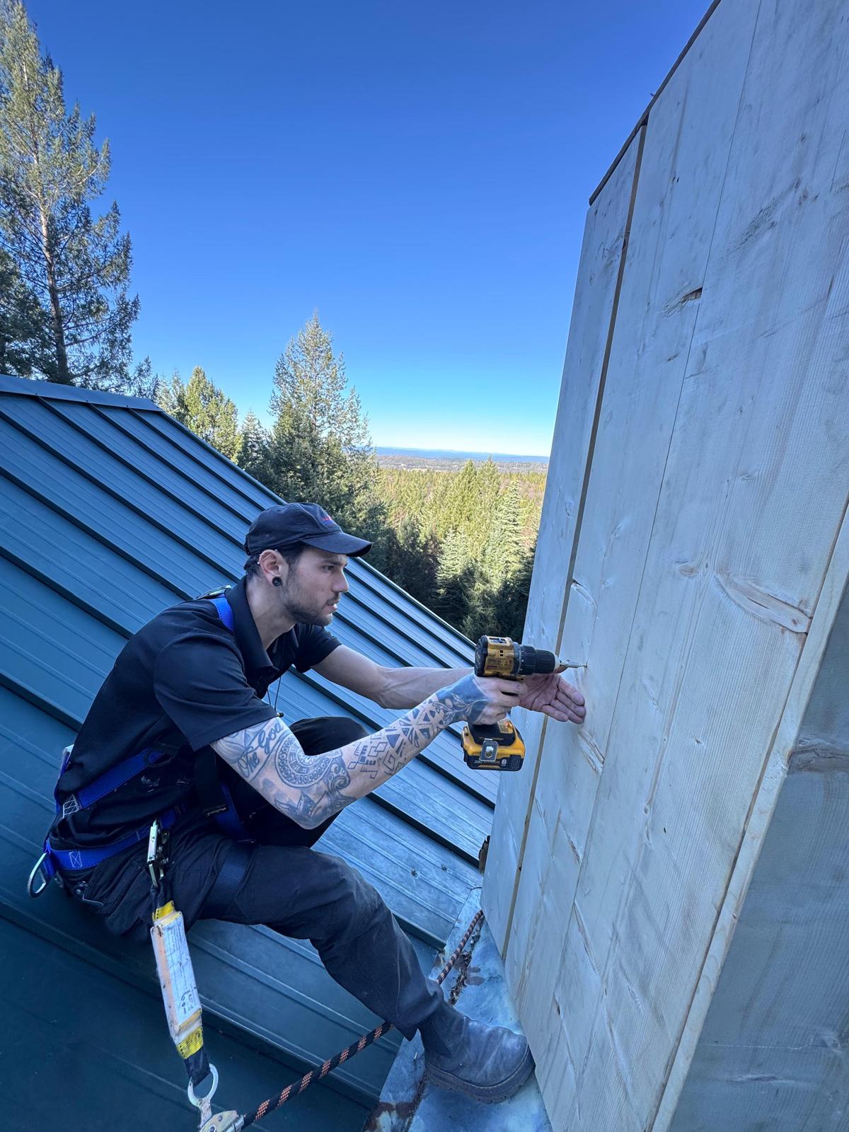 Michael in a fall-arrest harness drilling into a newly framed wood chimney chase